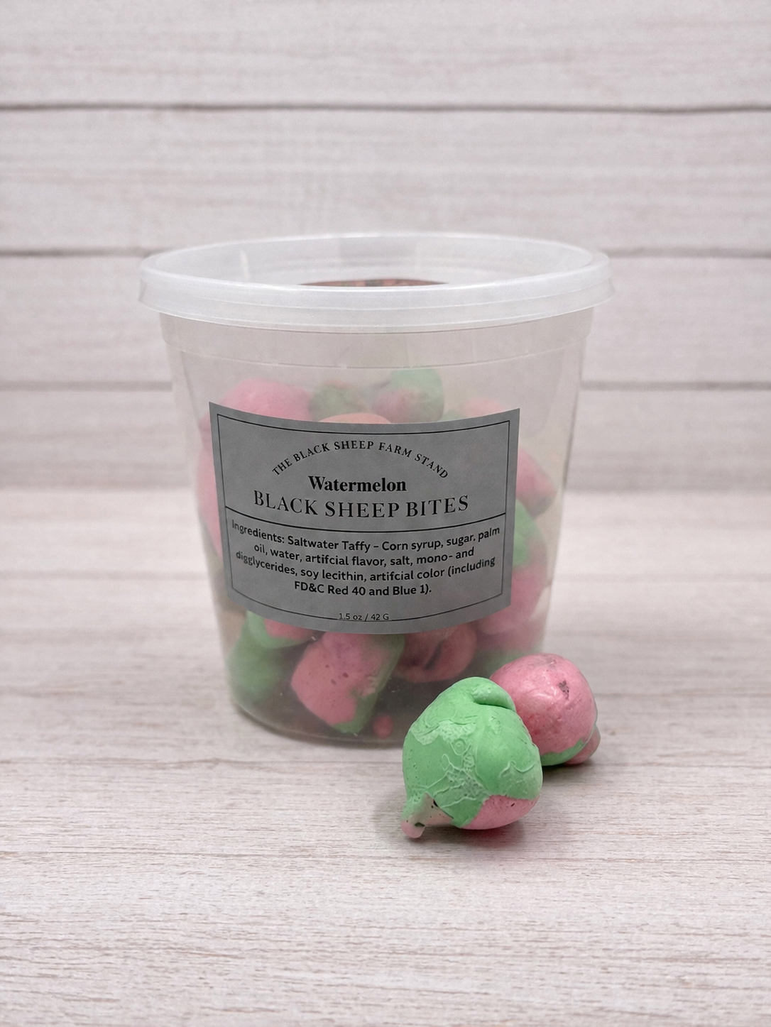 Clear container with pink and green treats labeled 'Black Sheep Bites' on a light wooden surface.