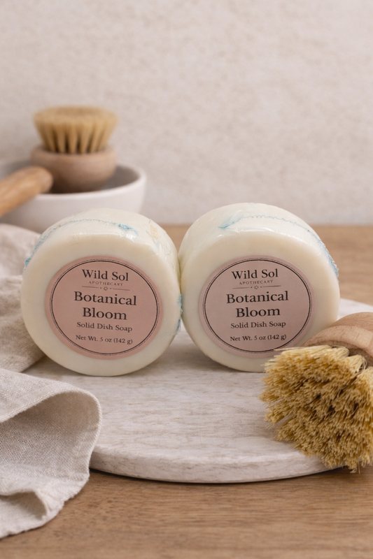2 Solid dish soaps on a stone with a dish brush. A dish brush and towel in the background