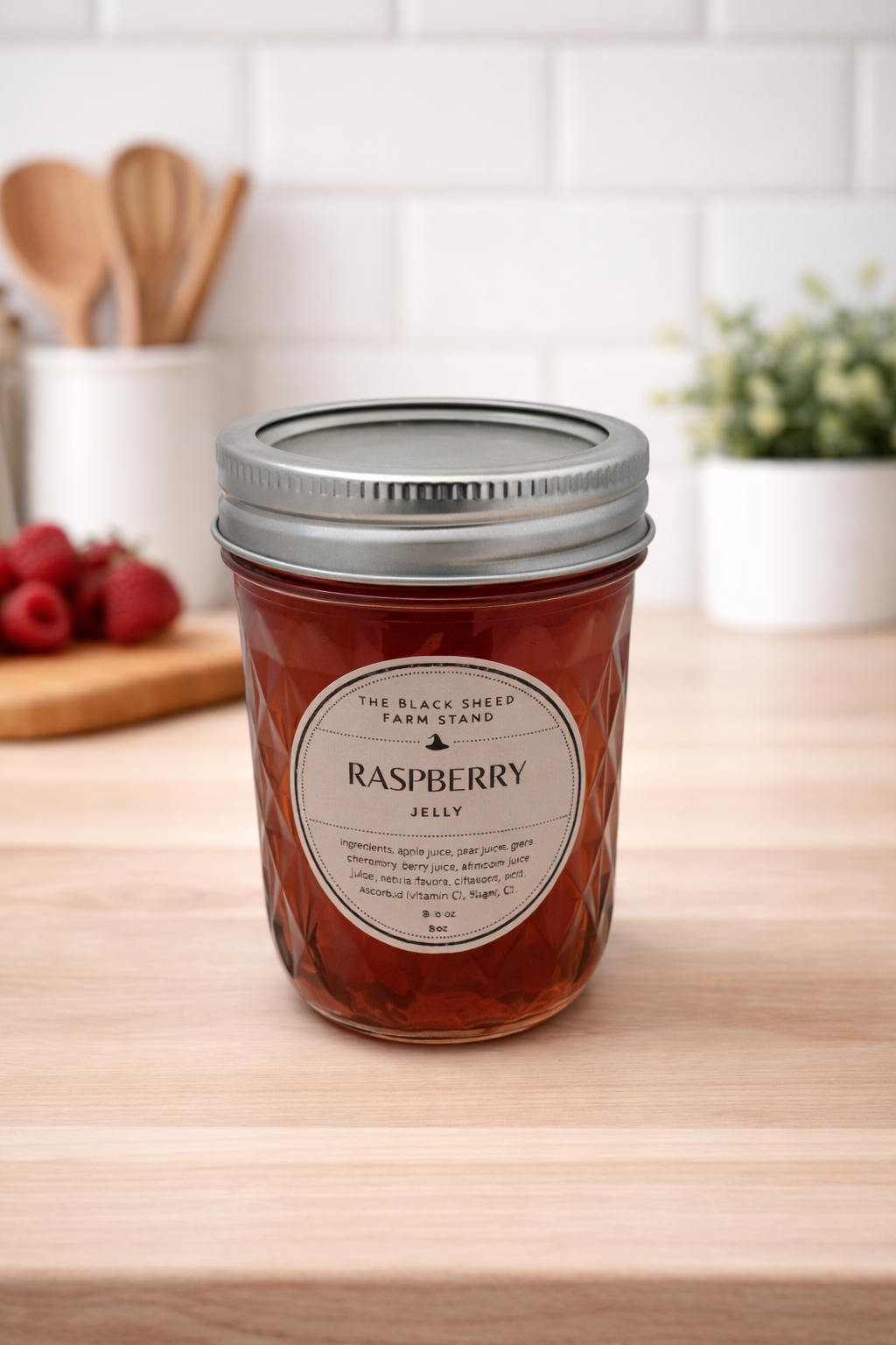 Jar of raspberry jelly on a kitchen counter with a white tiled wall and wooden utensils in the background.