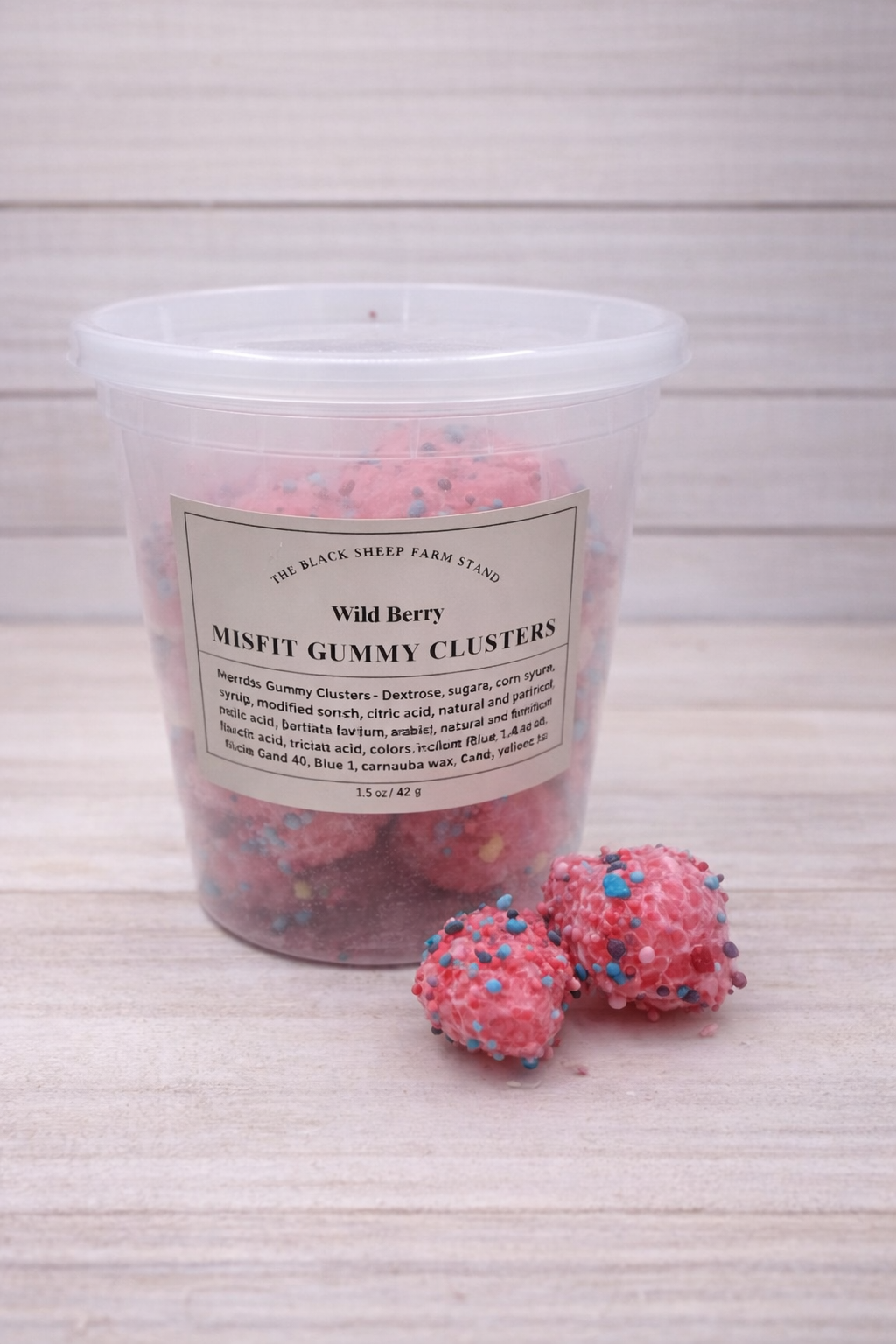 Container of Wild Berry Misfit Gummy Clusters with two gummies on a light wooden surface.
