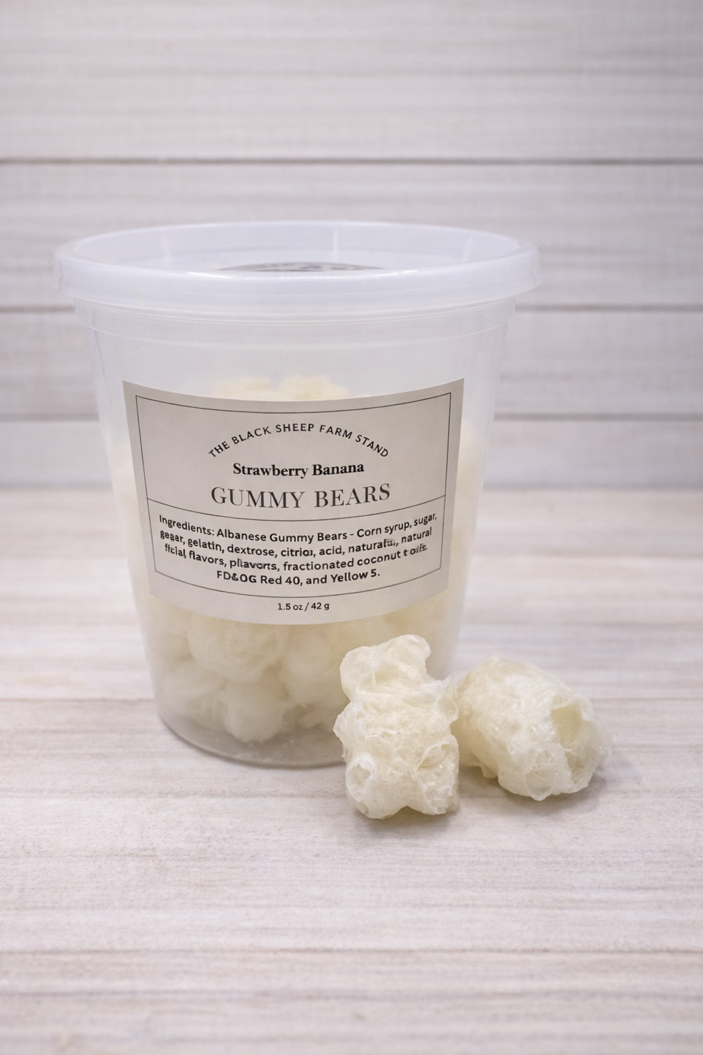 Jar of strawberry banana gummy bears with two gummy bears in front on a light wooden surface.