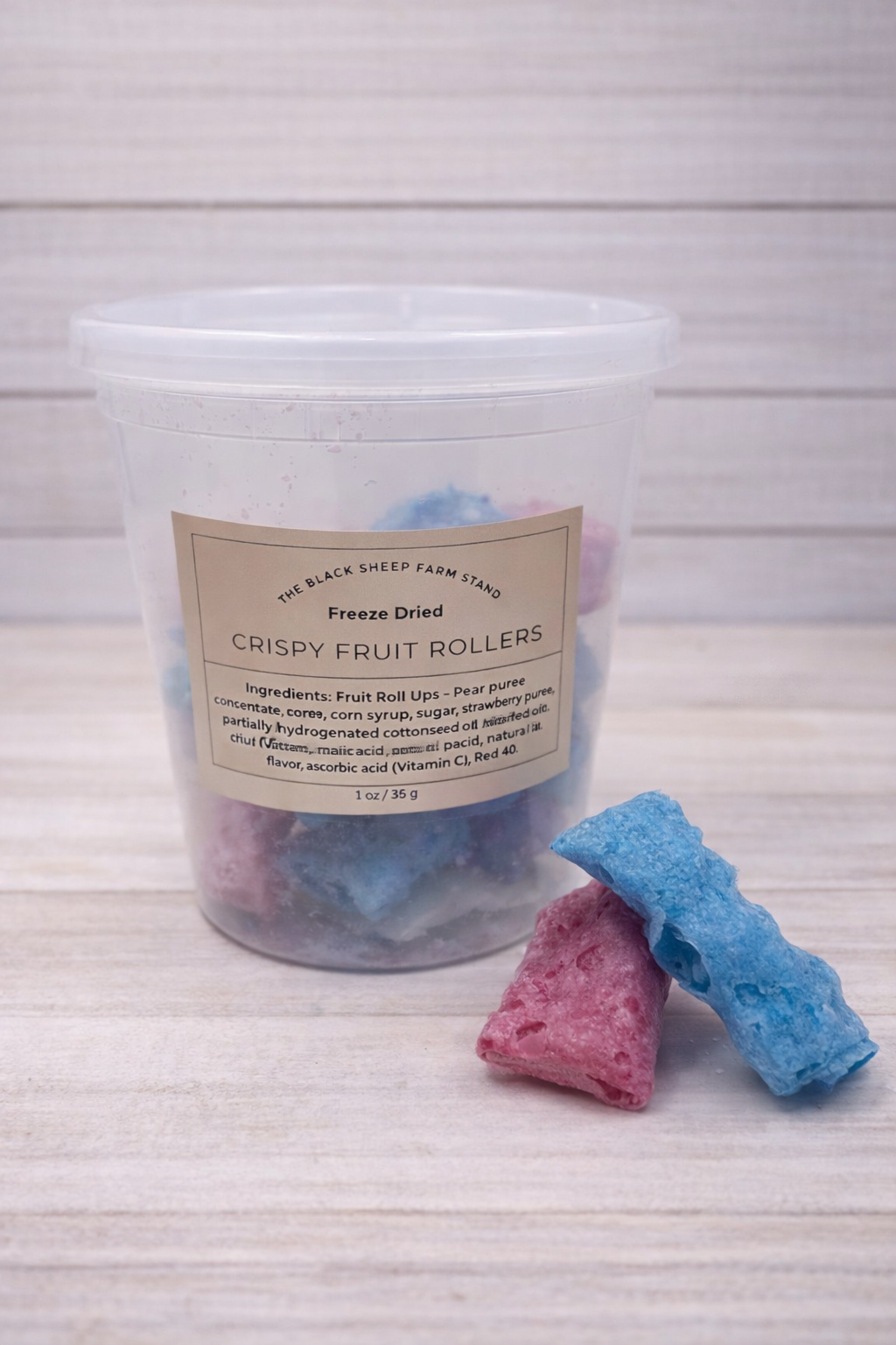 Container of freeze-dried crispy fruit rollers with two rolls on a white background